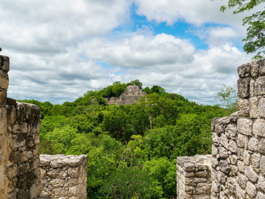 Calakmul ruins above the trees viewed through stone walls. In the Yucatan peninsula.