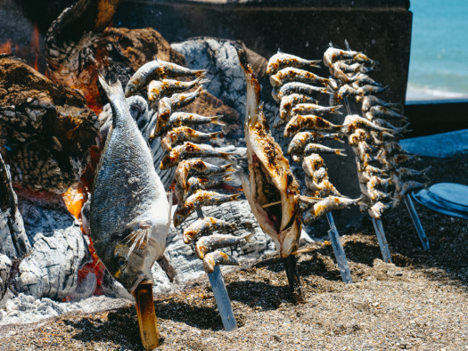 closeup of different espetos, skewers where fish is skewered, being cooked in a wood fire as its traditional in La Malagueta beach, in Malaga, Spain